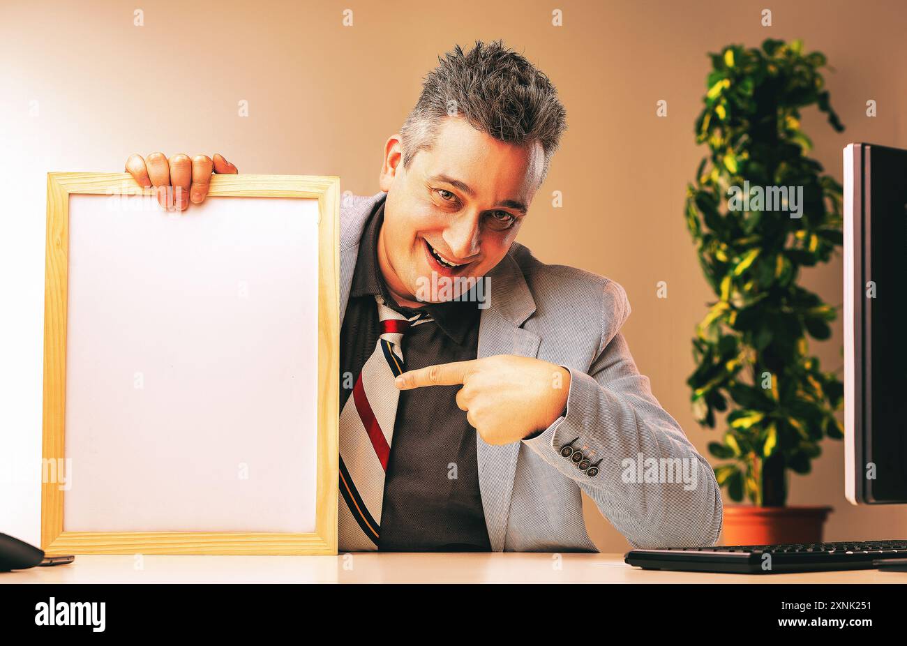 Un uomo d'affari subdolo in ufficio, che indica una lavagna con un sorriso sorridente, accennando a tattiche di vendita ombrose. Inganno, frode, comportamento non etico Foto Stock