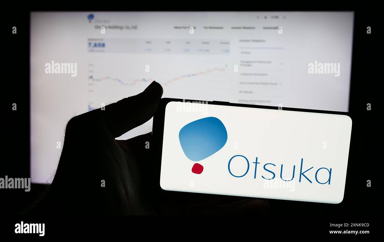 Persona che detiene un telefono cellulare con il logo della società giapponese Otsuka Pharmaceutical Co. Ltd. Di fronte alla pagina Web aziendale. Mettere a fuoco il display del telefono. Foto Stock