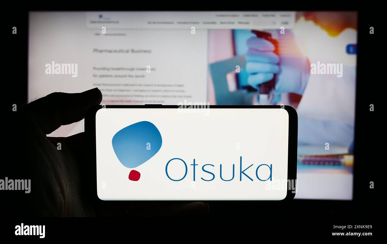 Persona che detiene un cellulare con il logo della società giapponese Otsuka Pharmaceutical Co. Ltd. Di fronte alla pagina Web aziendale. Mettere a fuoco il display del telefono. Foto Stock