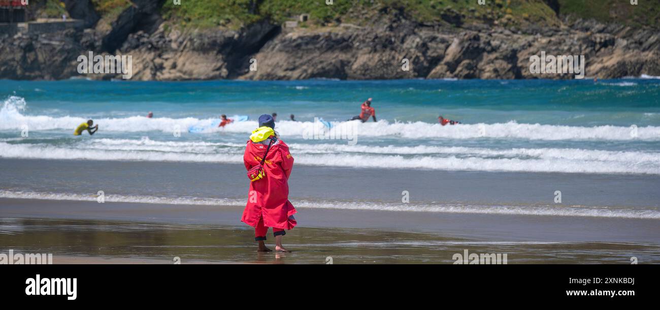 Un'immagine panoramica di un bagnino della Royal National Lifeboat Institution della RNLI in servizio sulla riva per osservare i surfisti principianti che praticano un lesso da surf Foto Stock