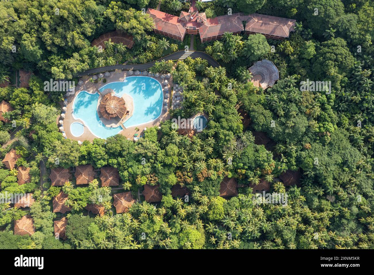 Paesaggio tropicale con tetti delle ville e piscina blu tra palme verdi vista aerea dei droni Foto Stock