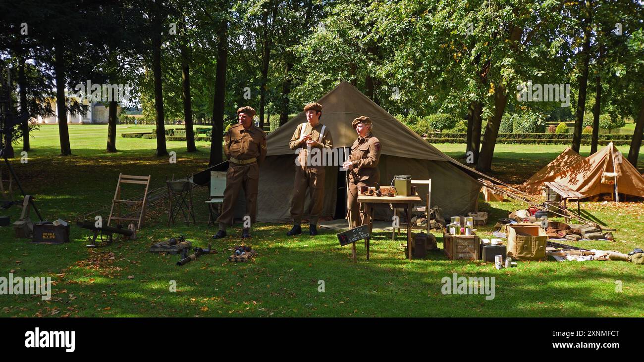 Persone in uniforme della seconda guerra mondiale in piedi in campo con tende sugli alberi. Foto Stock