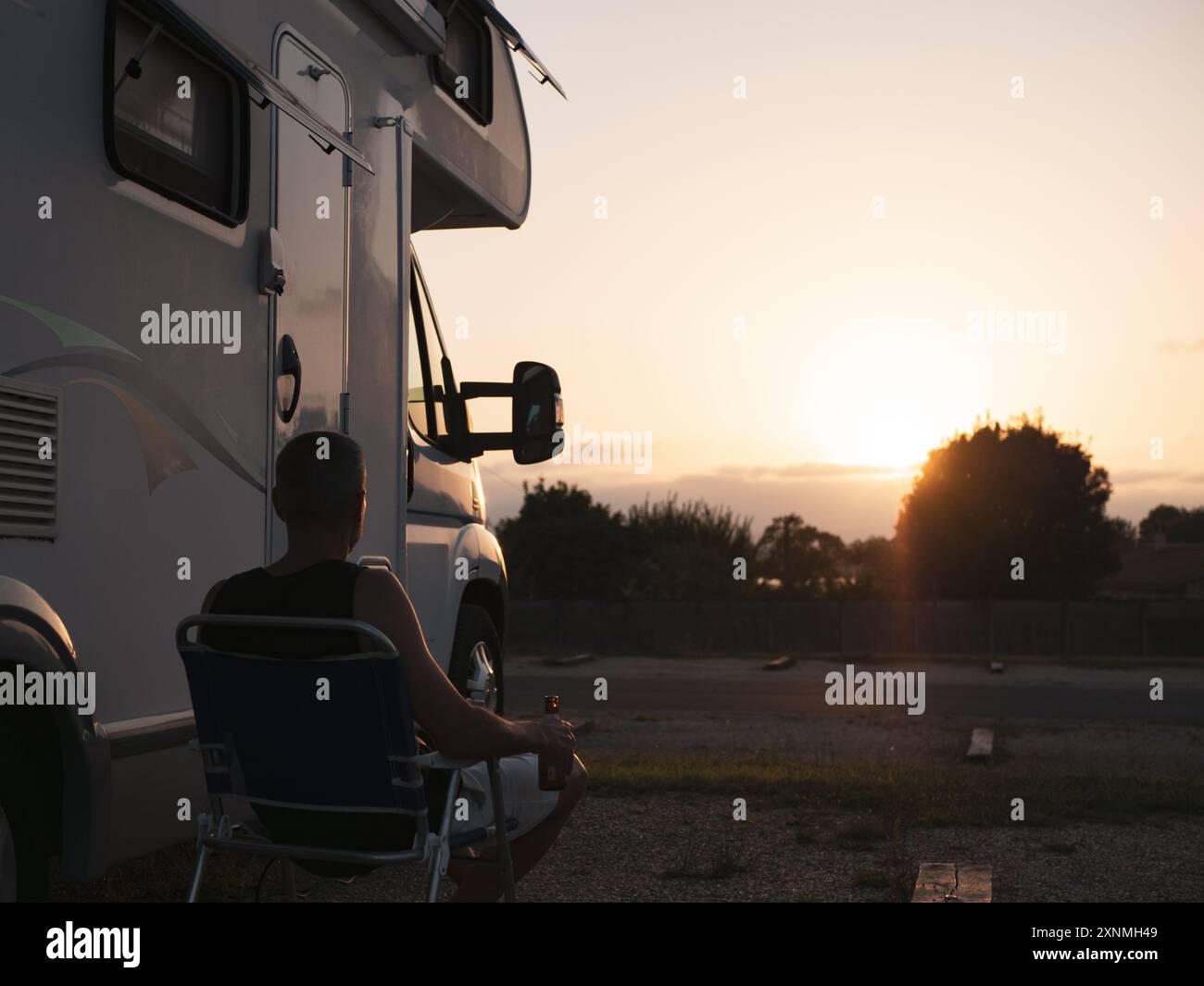 Uomo seduto fuori dal suo camper a bere una birra e a guardare il tramonto Foto Stock