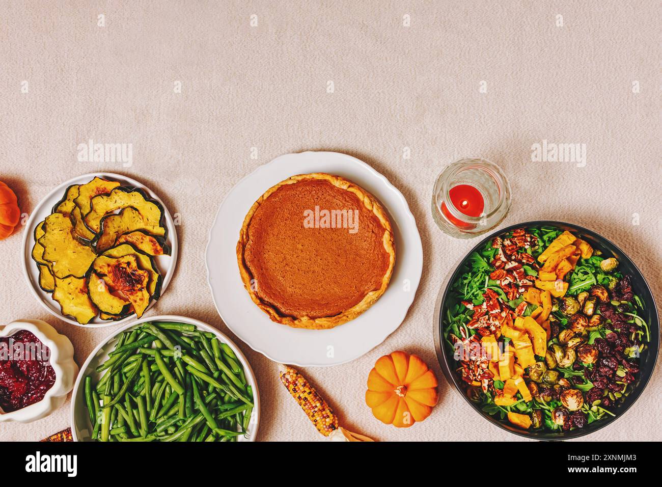Vista dall'alto del tavolo del Ringraziamento con torta di zucca fatta in casa, vivaci fagioli verdi, zucca arrosto e insalata fresca. Foto Stock