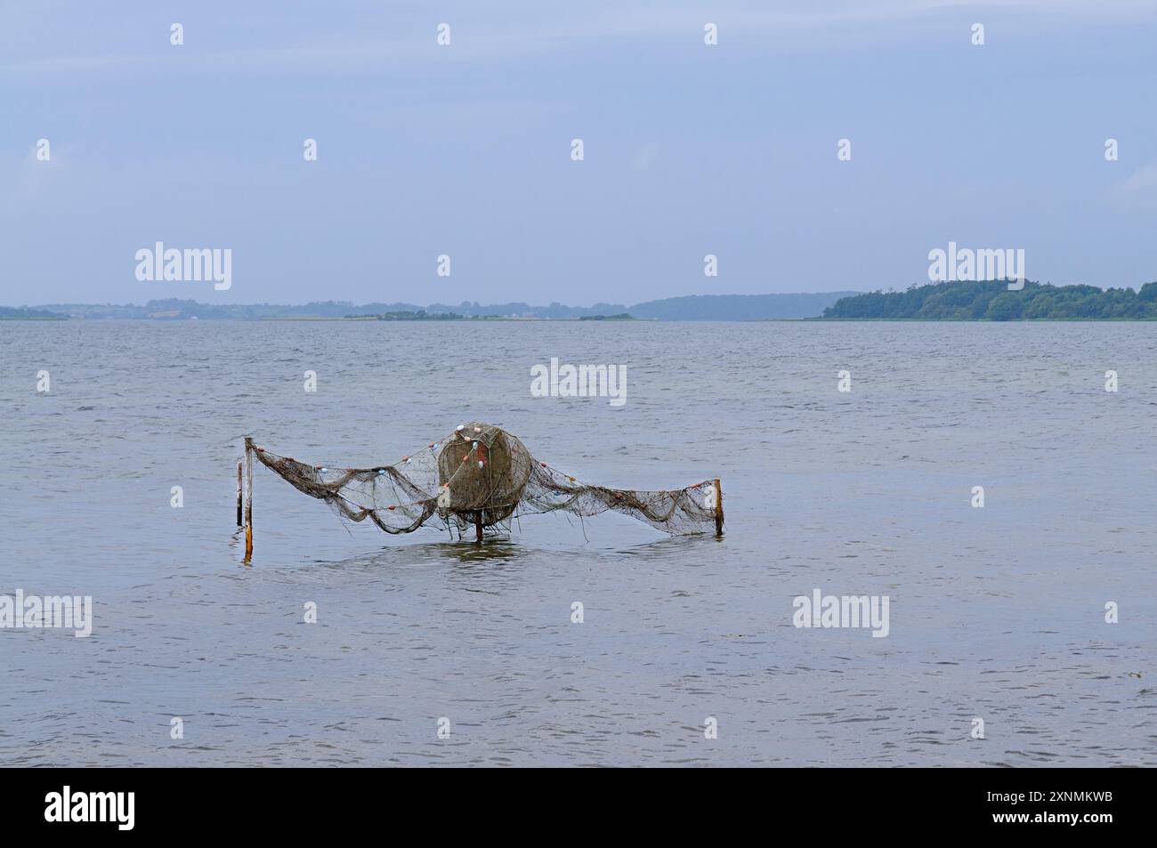 L'attrezzatura da pesca abbandonata galleggia dolcemente in acque tranquille, circondate da paesaggi sereni sotto un cielo blu morbido. Foto Stock