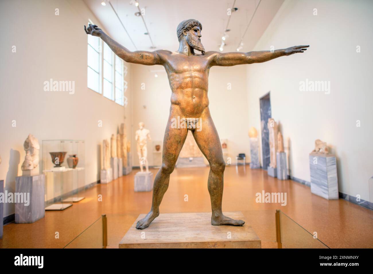 Zeus o statua di Poseidone Museo Archeologico Nazionale Atene // ATENE, Grecia — la statua di Zeus o Poseidone, una suggestiva scultura in bronzo del V secolo a.C., è una delle più famose mostre al Museo Archeologico Nazionale di Atene. Si ritiene che questa iconica scultura, scoperta nel mare al largo di Capo Artemision, rappresenti Zeus, che regge un fulmine, o Poseidone, che brandisce un tridente. La statua è celebrata per la sua posa dinamica e l'intricata maestria artigianale, che esemplifica l'eccellenza artistica degli antichi scultori greci. Foto Stock