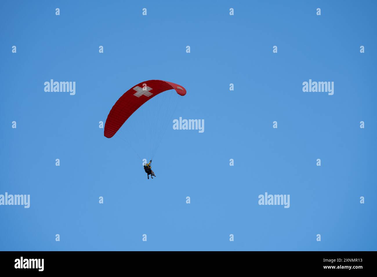 Parapendio in tandem contro un cielo blu vicino a Murren in Svizzera nell'Oberland Bernese, paracadute con bandiera svizzera Foto Stock