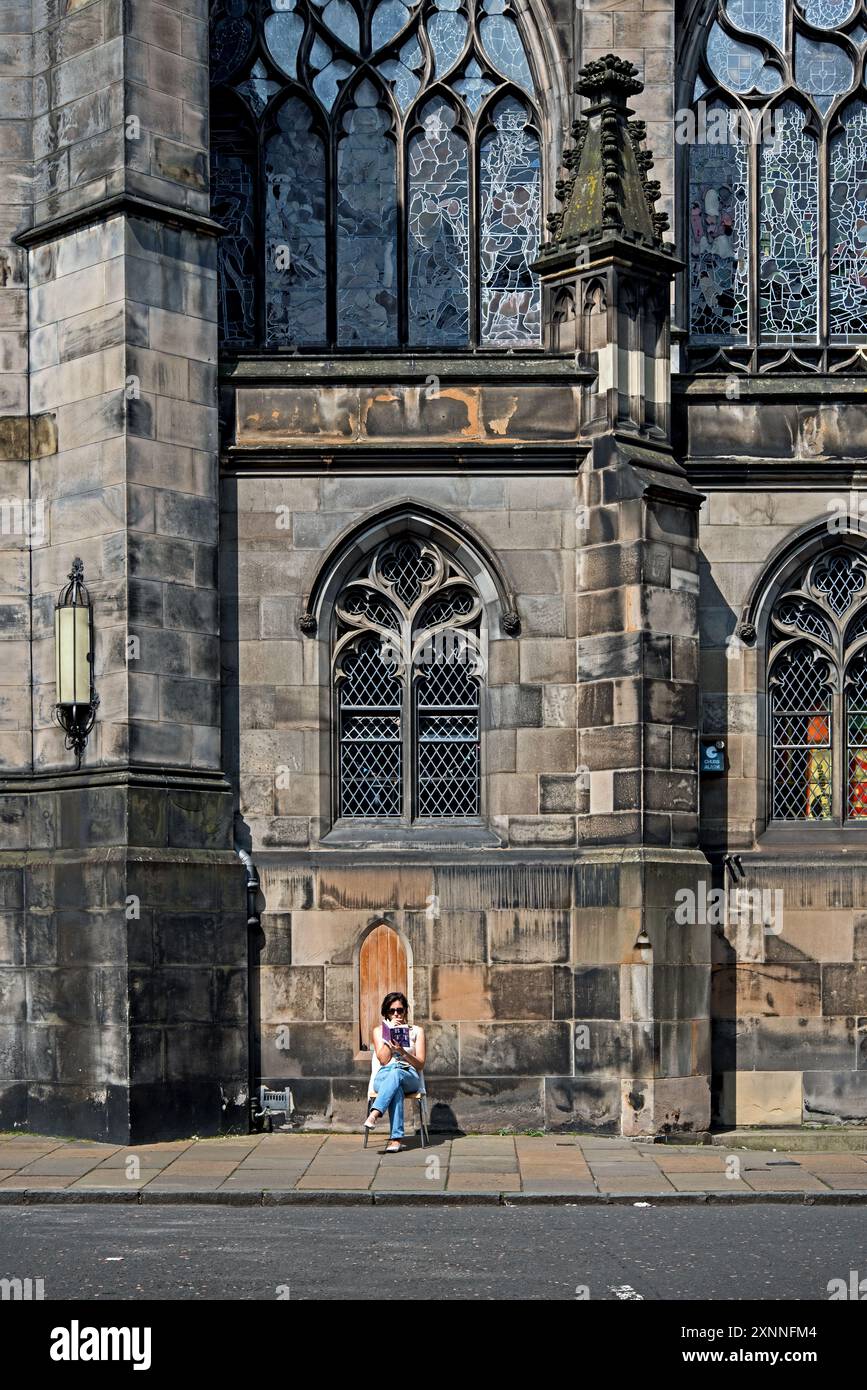 Giovane donna seduta a leggere al sole in Parliament Square nella città vecchia di Edimburgo. Foto Stock