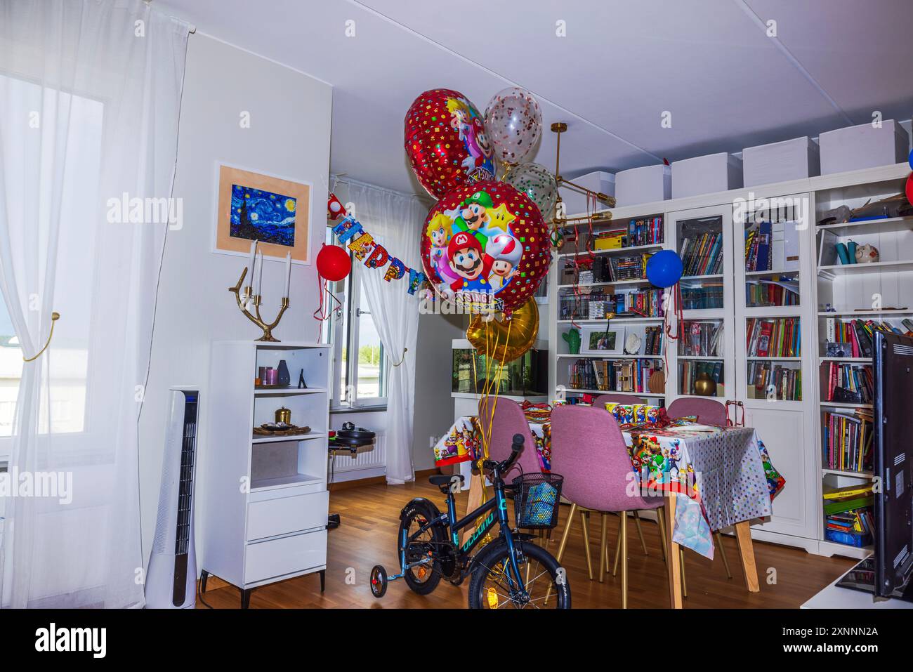 Splendida vista della camera arredata per il compleanno dei bambini, dotata di bicicletta confezionata in regalo con palloncini a tema Mario. Foto Stock