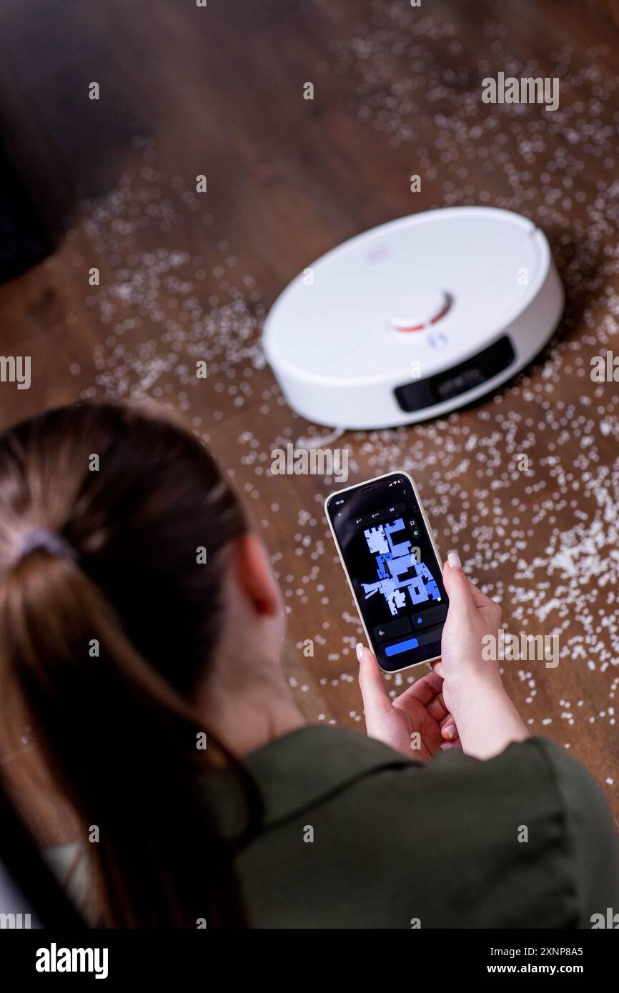 Giovane donna che usa lo smartphone per controllare l'aspirapolvere robot intelligente Foto Stock