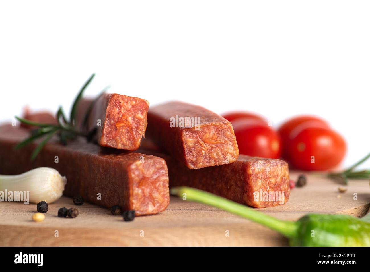 Bastoncini di salsiccia gustosi e piccanti presentati su una tavola di legno, circondati da ingredienti freschi, tra cui spicchi d'aglio, erbe verdi, grani di pepe nero, a. Foto Stock