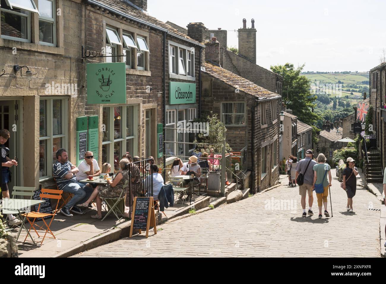 Persone sedute fuori da un caffè a Howarth Main Street, Yorkshire, Inghilterra, Regno Unito Foto Stock