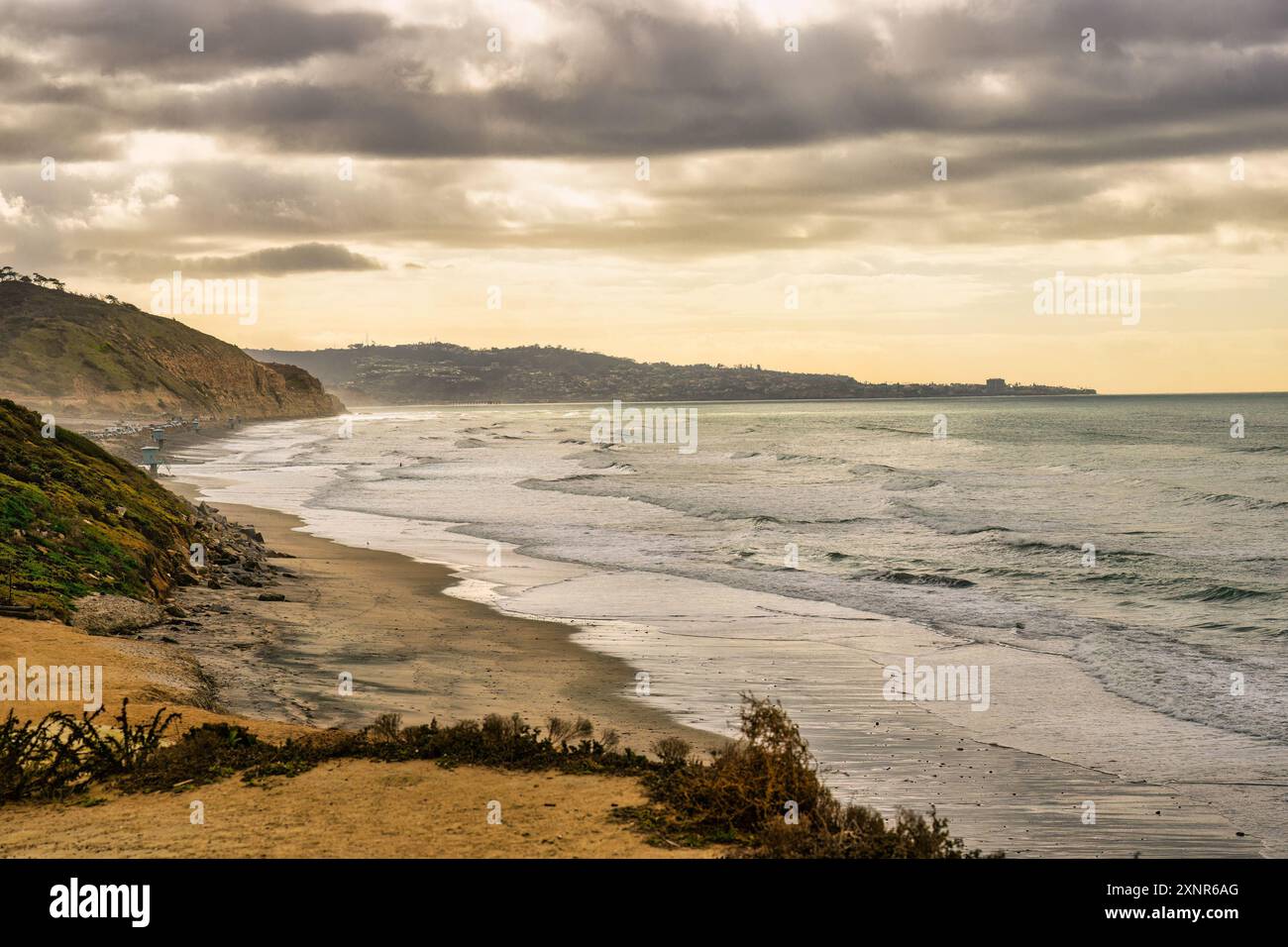 Paesaggio costiero panoramico al tramonto con onde che si infrangono sulla spiaggia e scogliere sullo sfondo della spiaggia statale di Torrey Pines Foto Stock