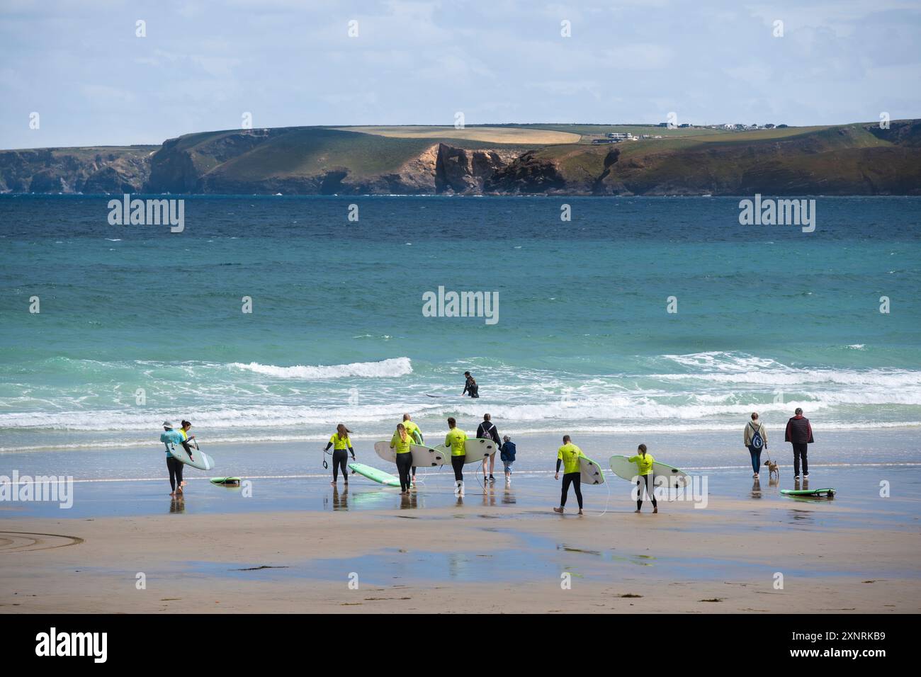 Un istruttore di surf della Escape Surf School e un gruppo di principianti che camminano in mare per una lezione di surf a Towan Beach a Newquay, Cornwa Foto Stock