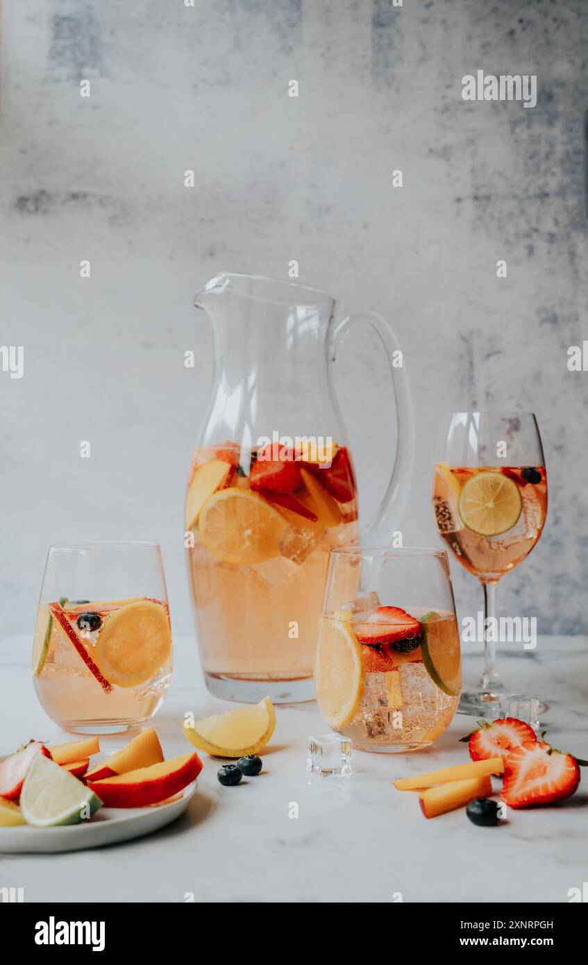 Caraffa e bicchieri di sangria bianca con frutta su marmo bianco. Foto Stock