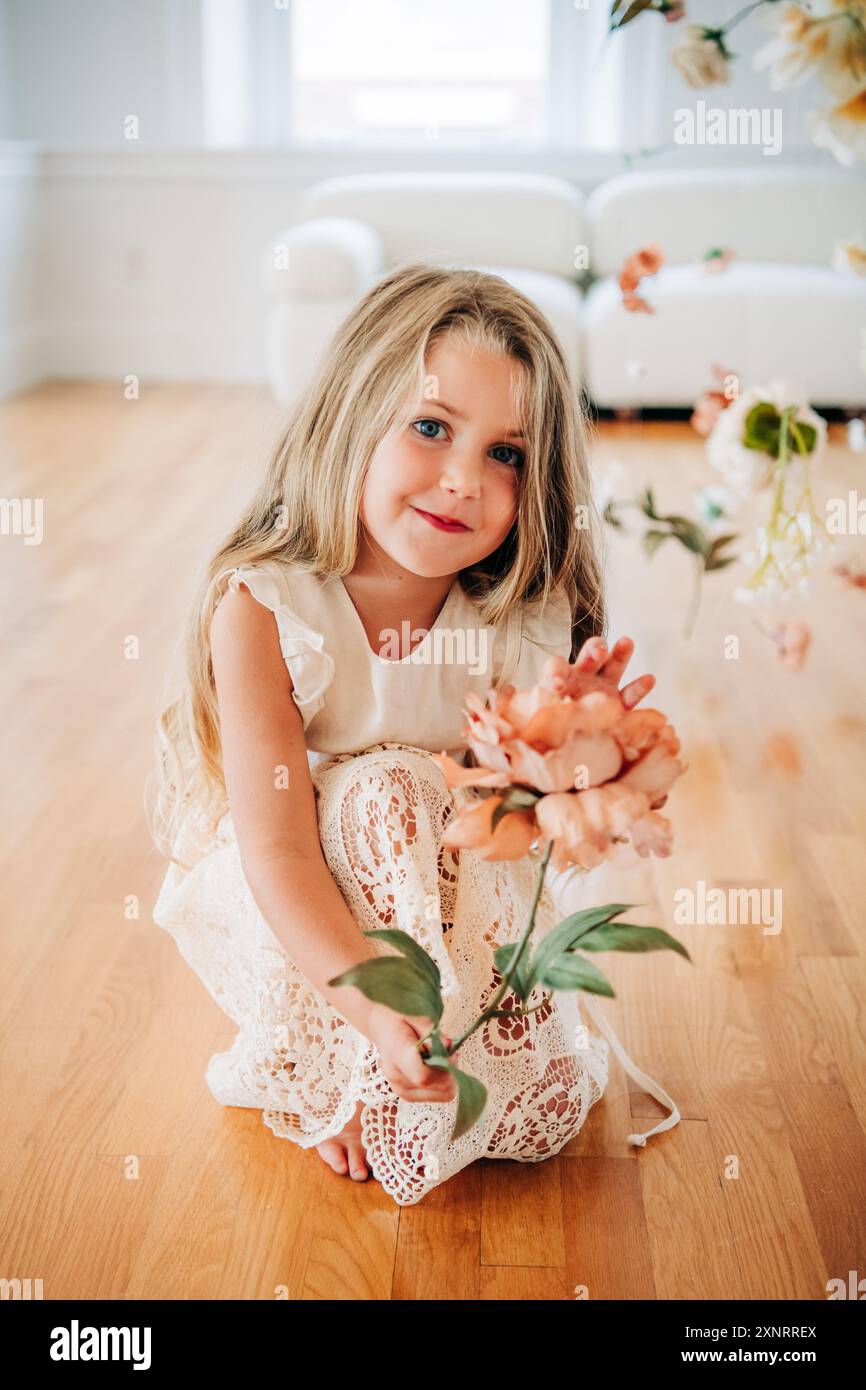 Ragazza bionda in abito in pizzo che tiene fiori, sorride in casa Foto Stock