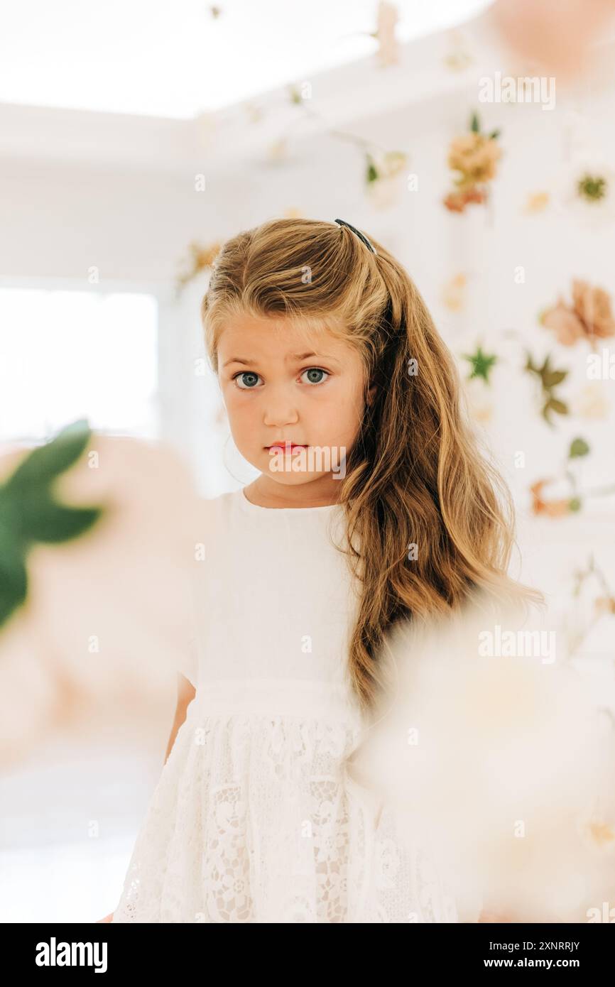 Ragazza bionda in abito bianco tra fiori guarda curiosamente avanti Foto Stock