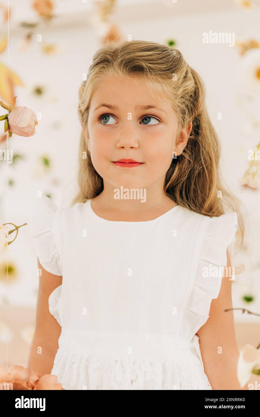 Ragazza bionda in abito bianco tra fiori guarda di lato Foto Stock