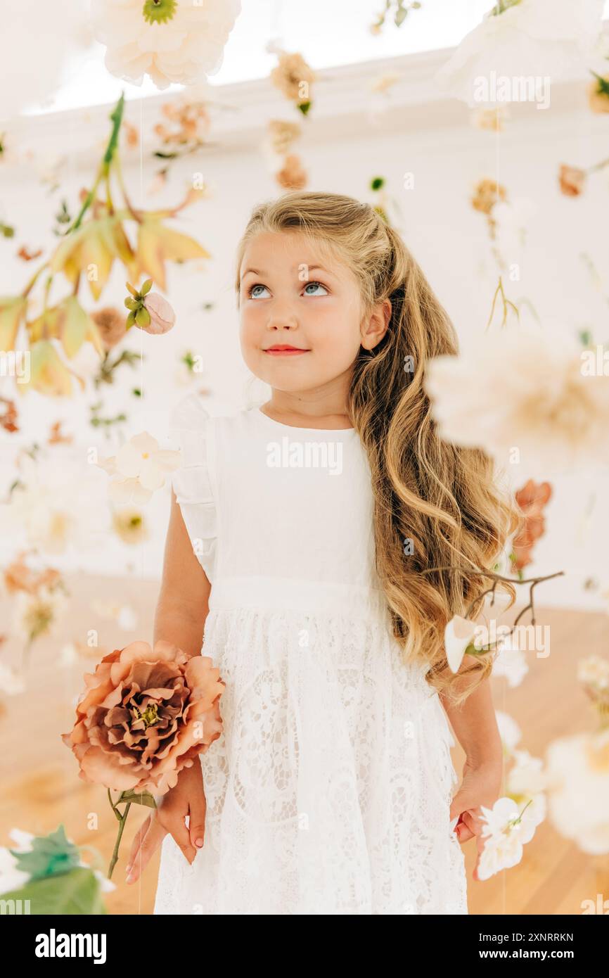Ragazza bionda in abito bianco tra fiori guarda sorridente Foto Stock