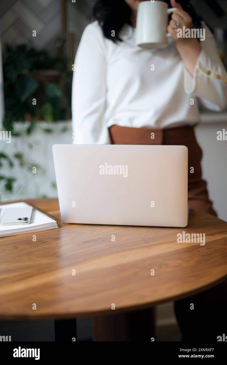 Donna che beve caffè, laptop su un tavolo di legno, ambiente interno. Foto Stock