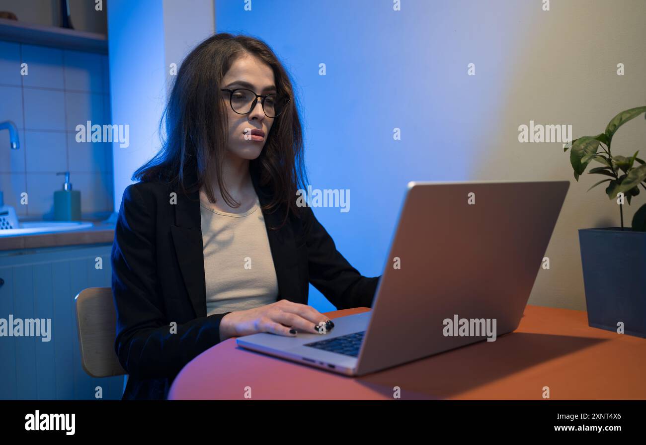 Donna d'affari concentrata che lavora su un notebook in una cucina moderna di notte. Foto Stock