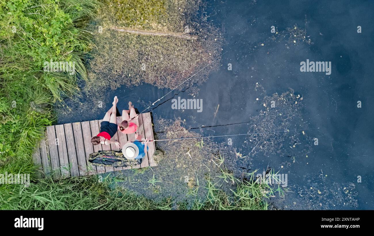 Famiglia e amici felici che pescano insieme all'aperto vicino al lago in estate, vista dall'alto Foto Stock