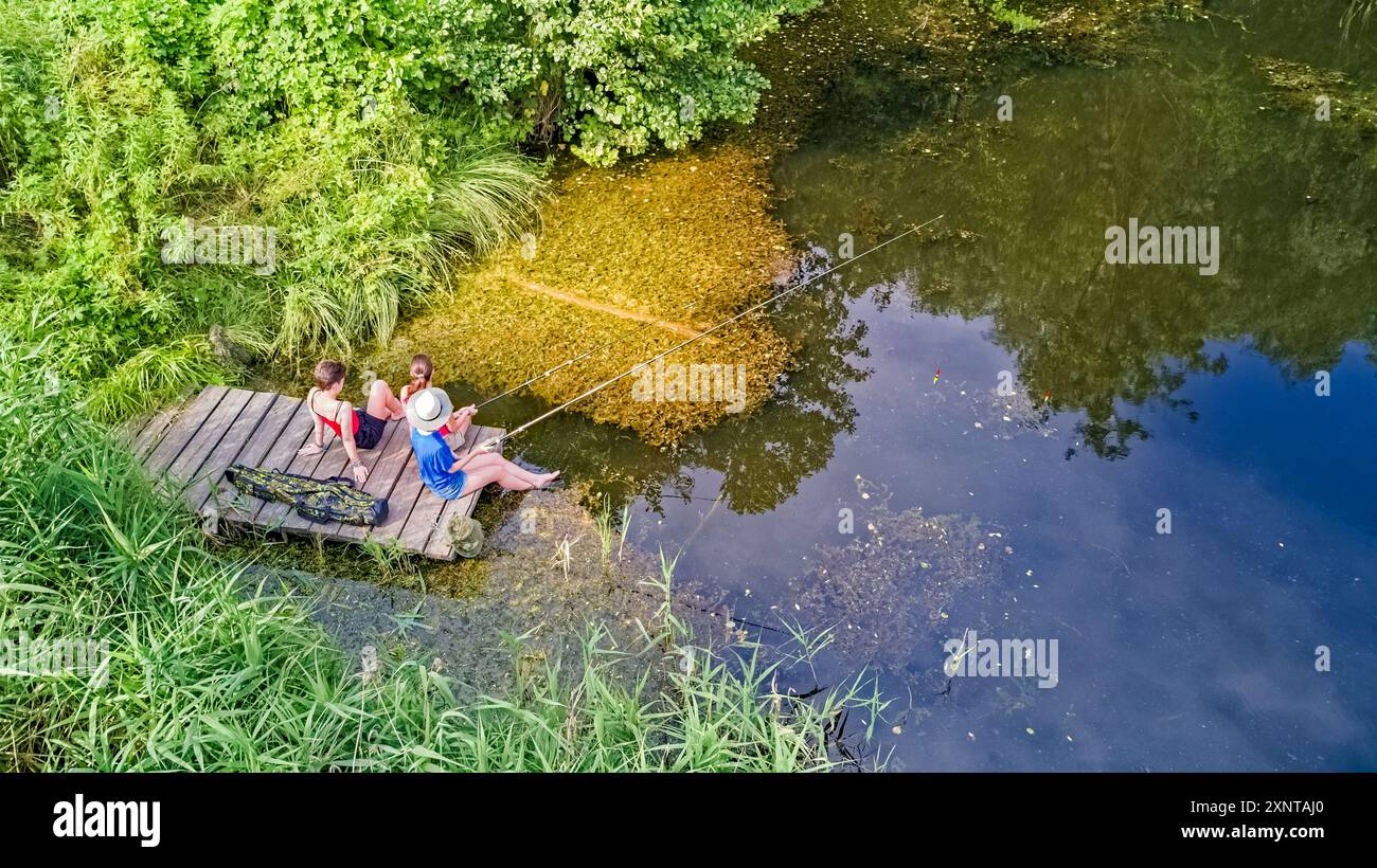 Famiglia e amici felici che pescano insieme all'aperto vicino al lago in estate, vista dall'alto Foto Stock