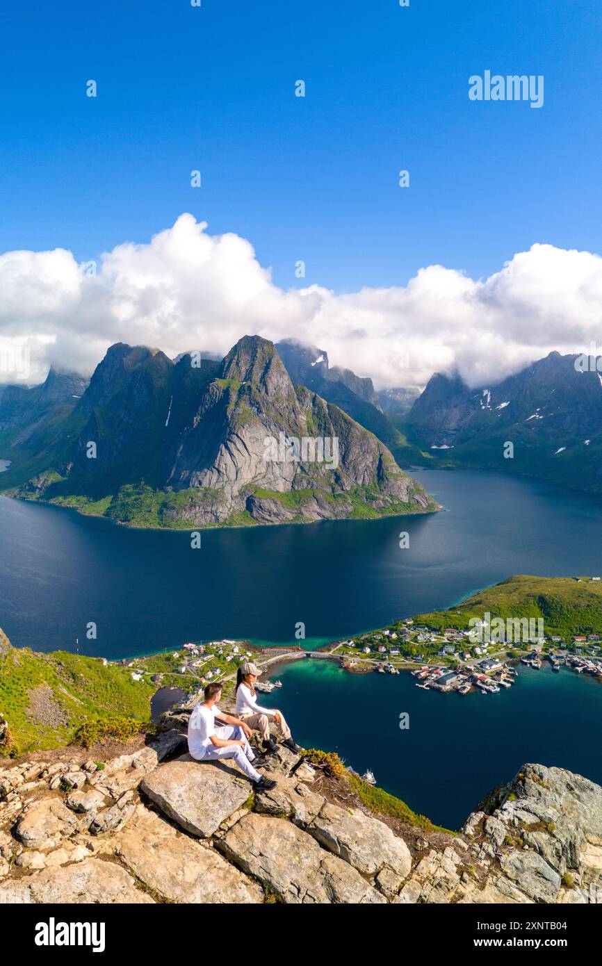 Due escursionisti godono della vista mozzafiato di un fiordo circondato da montagne sotto un cielo azzurro. Reinebringen Lofoten Norvegia Foto Stock