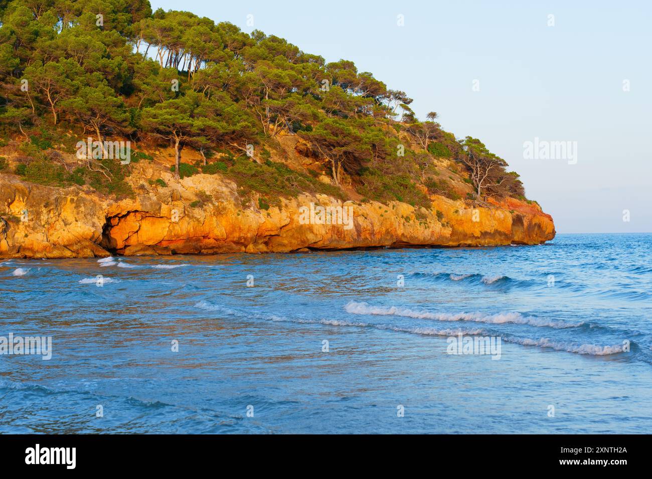 Vista mozzafiato della costa rocciosa che si fonde con le acque cristalline e la lussureggiante vegetazione che incornicia la riva e che esalta la bellezza naturale di Ta Foto Stock