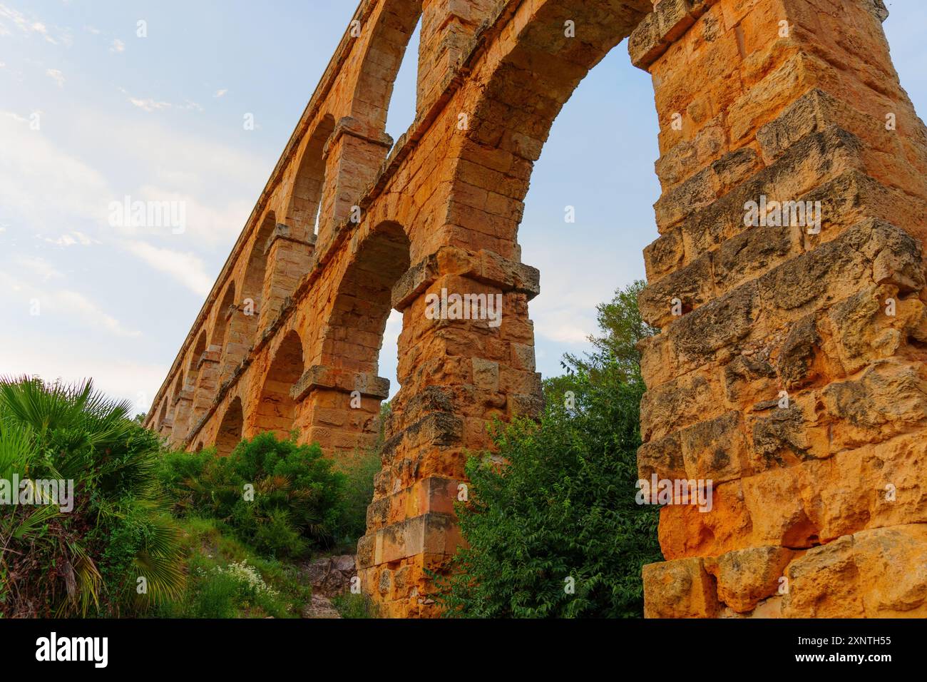 La vista laterale del Ponte del Diavolo mette in risalto intricati lavori in pietra e ampi archi, circondati da una vivace vegetazione al tramonto. Foto Stock