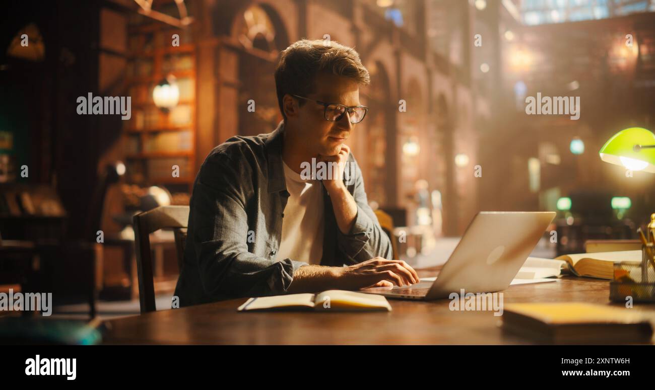 Giovane studente maschio caucasico impegnato nell'e-learning con laptop in un ambiente di biblioteca d'epoca, circondato da libri e da un'illuminazione calda Foto Stock