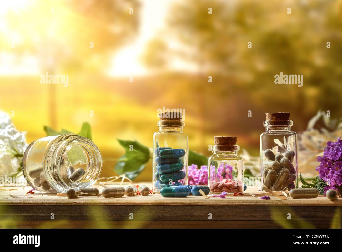 Medicinali vegetali naturali con capsule e pillole in vasetti di vetro su tavola di legno con fiori in natura. Vista frontale. Foto Stock