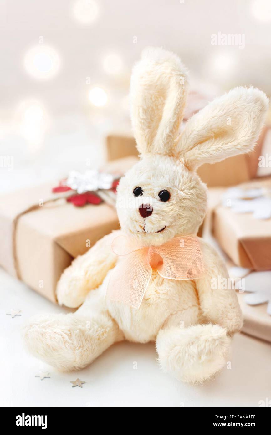 Regali avvolti con coniglio peluche giocattolo, simbolo del Capodanno 2023. Decorazioni per l'albero di Natale su sfondo festivo. Biglietto d'auguri per le festività. Foto Stock