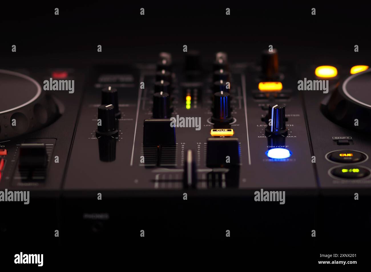 Un DJ mixer nero con vari pulsanti e manopole, illuminato su uno sfondo scuro, che crea un'atmosfera ritmica e professionale, mixa l'audio dj Foto Stock