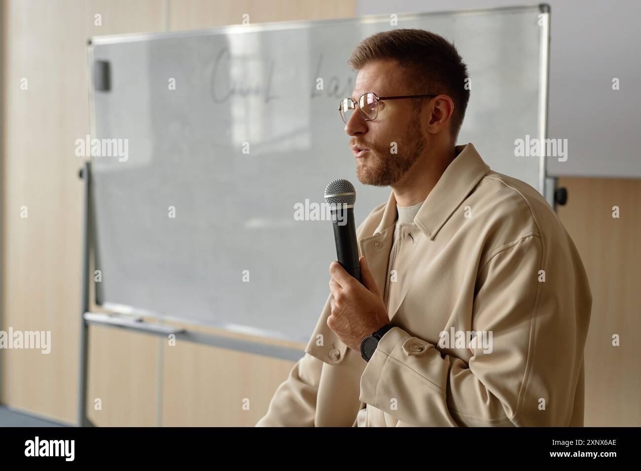 Vista laterale ritratto del professore di sesso maschile adulto in occhiali che tiene una lezione di legge parlando con microfono portatile in classe universitaria, spazio di copia Foto Stock