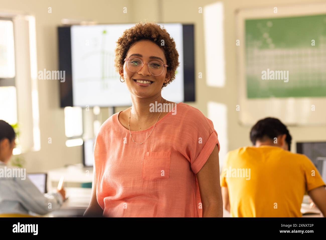 Insegnante sorridente in classe con studenti che lavorano su notebook alle superiori Foto Stock