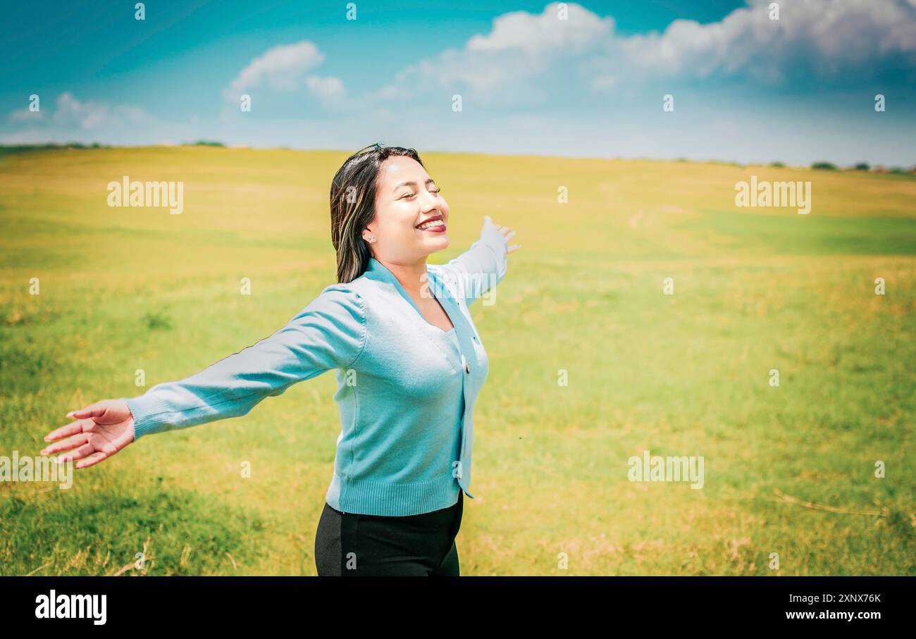 Giovane donna serena che respira aria fresca in un bellissimo campo che si allarga le braccia. Ragazza felice che si spalanca le braccia respirando aria fresca nel campo Foto Stock