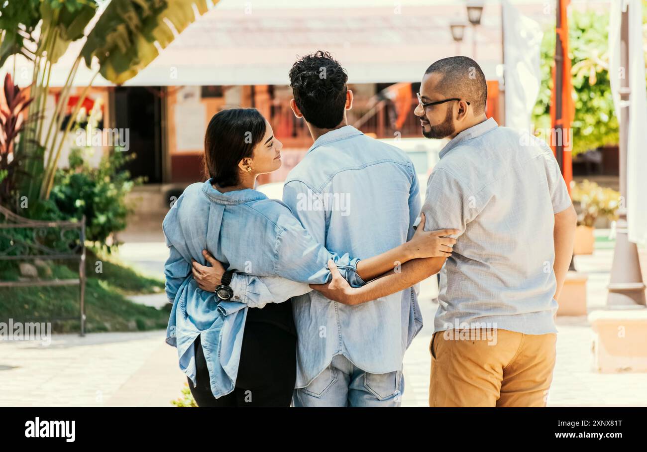 Ragazza infedele che cammina nel parco con il suo ragazzo mentre tiene un altro uomo per mano. Donna che si tiene per mano con un altro uomo mentre cammina con lei Foto Stock