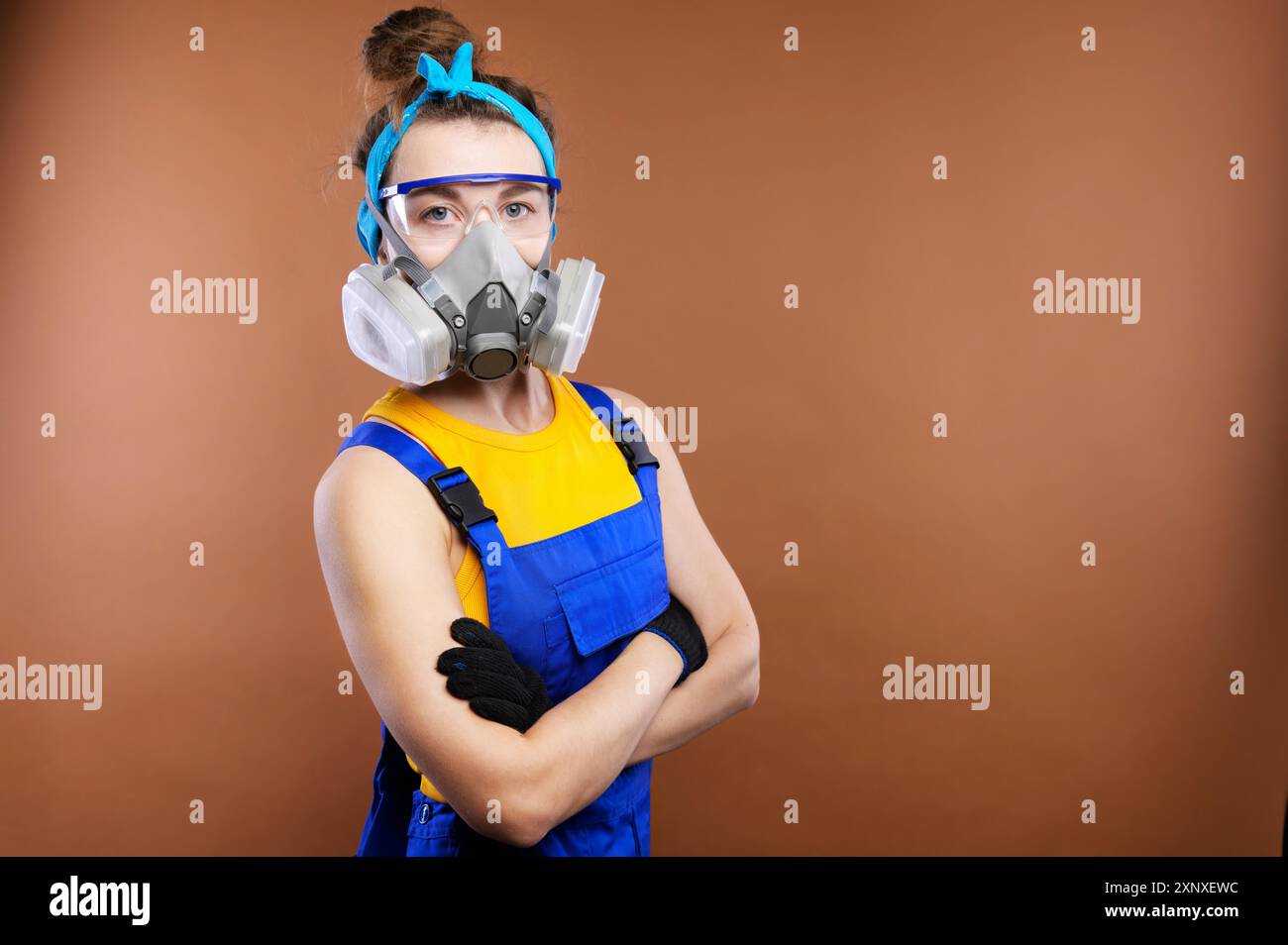Ritratto di una giovane donna caucasica costruttore. Le braccia sono piegate sul torace. Indossare occhiali protettivi e un respiratore con maschera respiratoria. Foto Stock