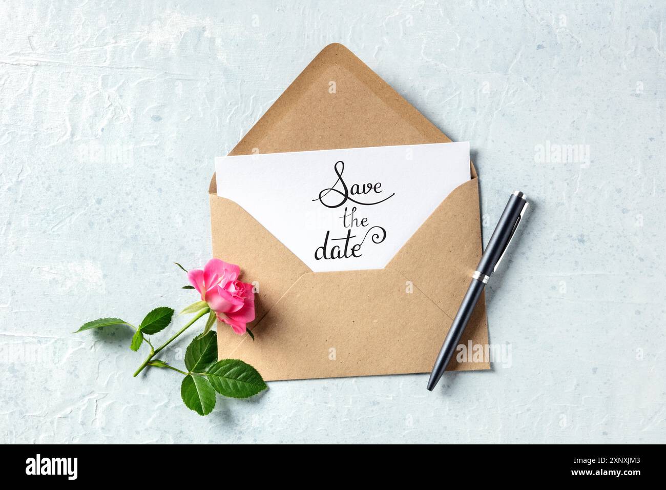Salva l'indicazione della data su un invito in una busta marrone kraft, girato dall'alto con una rosa Foto Stock