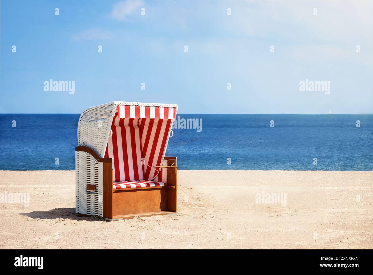 Sedia da spiaggia in vimini con strisce rosse e bianche sulla spiaggia di sabbia del Mar Baltico contro l'acqua e il cielo blu, biglietto d'auguri per le vacanze estive, copia Foto Stock