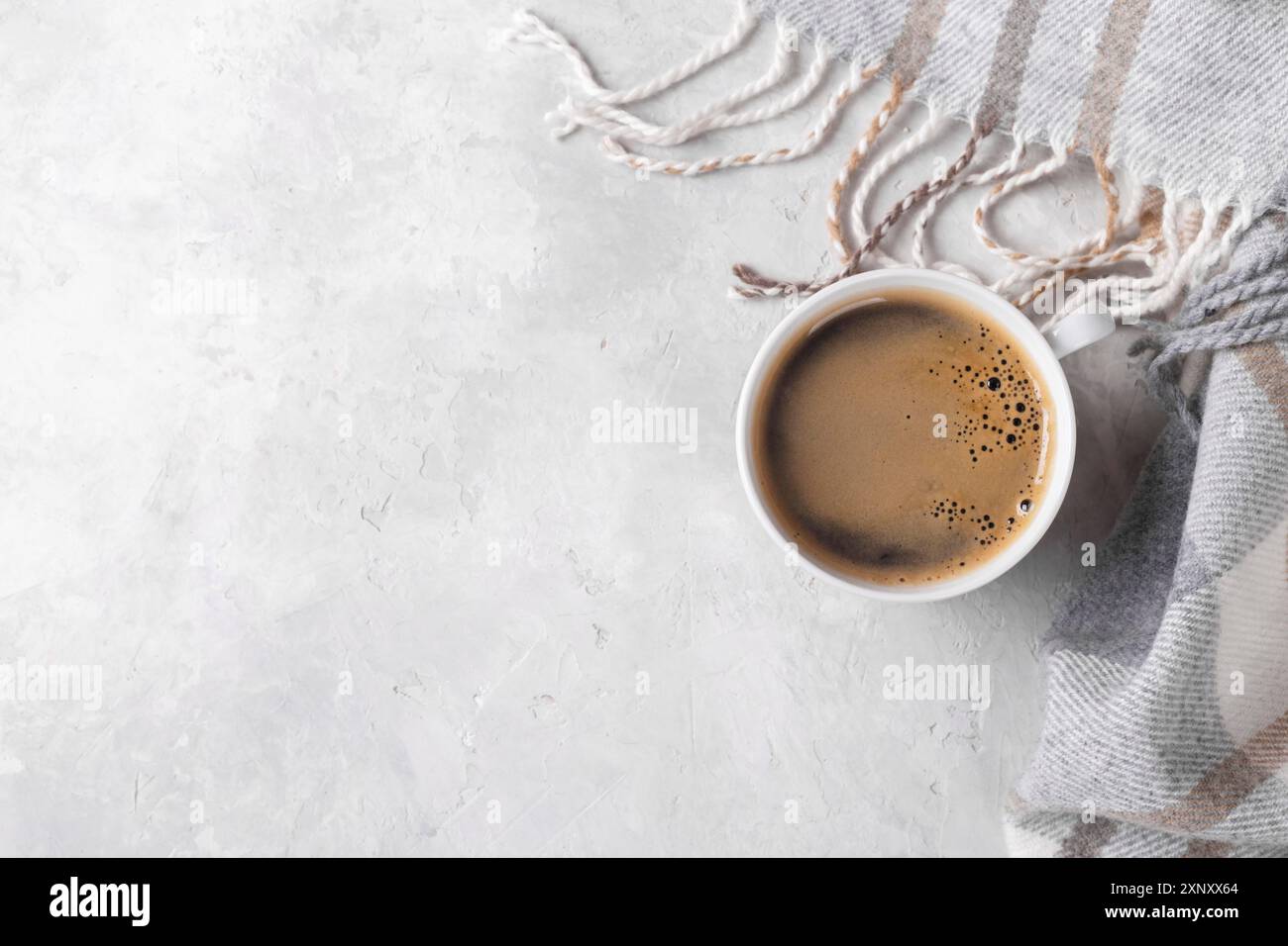 Tazza di caffè caldo e plaid a scacchi su sfondo grigio pietra copia spazio piatto vista dall'alto Foto Stock
