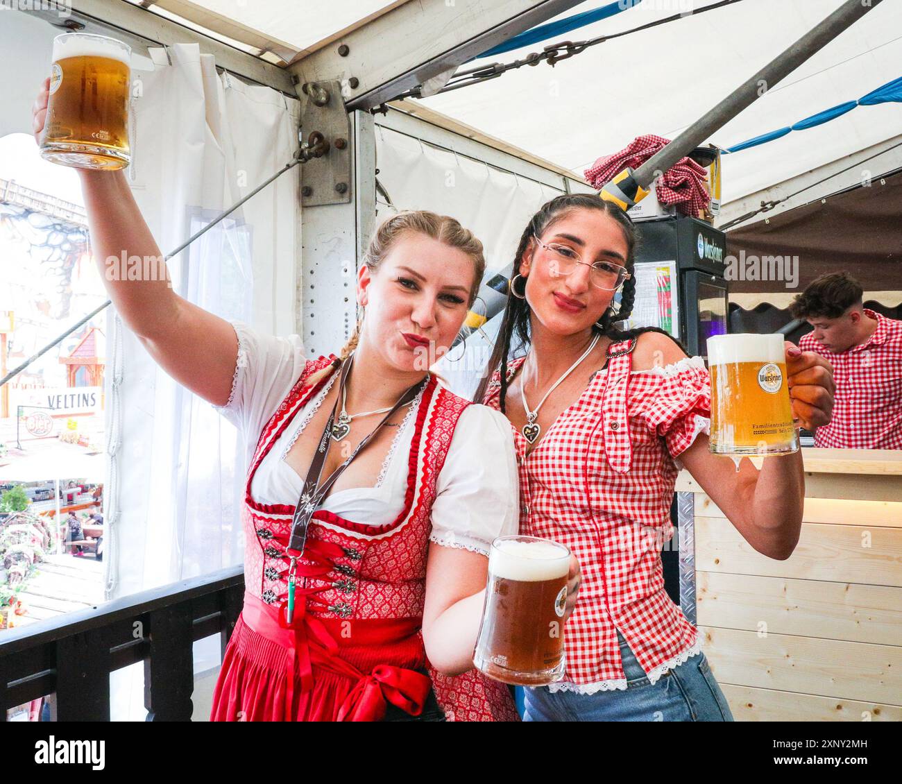 Herne, NRW, Germania. 2 agosto 2024. Due cameriere servono con un sorriso. Cranger Kirmes, la seconda fiera più grande della Germania (dopo l'Oktoberfest di Monaco), si apre con la tradizionale spillatura del barile, effettuata dal sindaco Frank Dudda, dal vice PM dell'NRW Mona Neubaur e da altri, oltre all'intrattenimento della cantante tedesca Vanessa mai. La vivace fiera ha una lunga tradizione che risale al XV secolo, dove un mercato di cavalli e successivamente intrattenitori medievali, legnavano la folla. Cranger Kirmes attrae circa 4 milioni di visitatori ogni anno in un sito dedicato lungo il canale Reno-Herne. Foto Stock