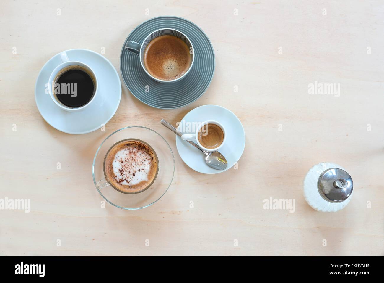 Varie bevande a base di caffè come espresso, cappuccino, lungo nero e crema e un distributore di zucchero su un tavolo di legno chiaro, formato panoramico, copia Foto Stock