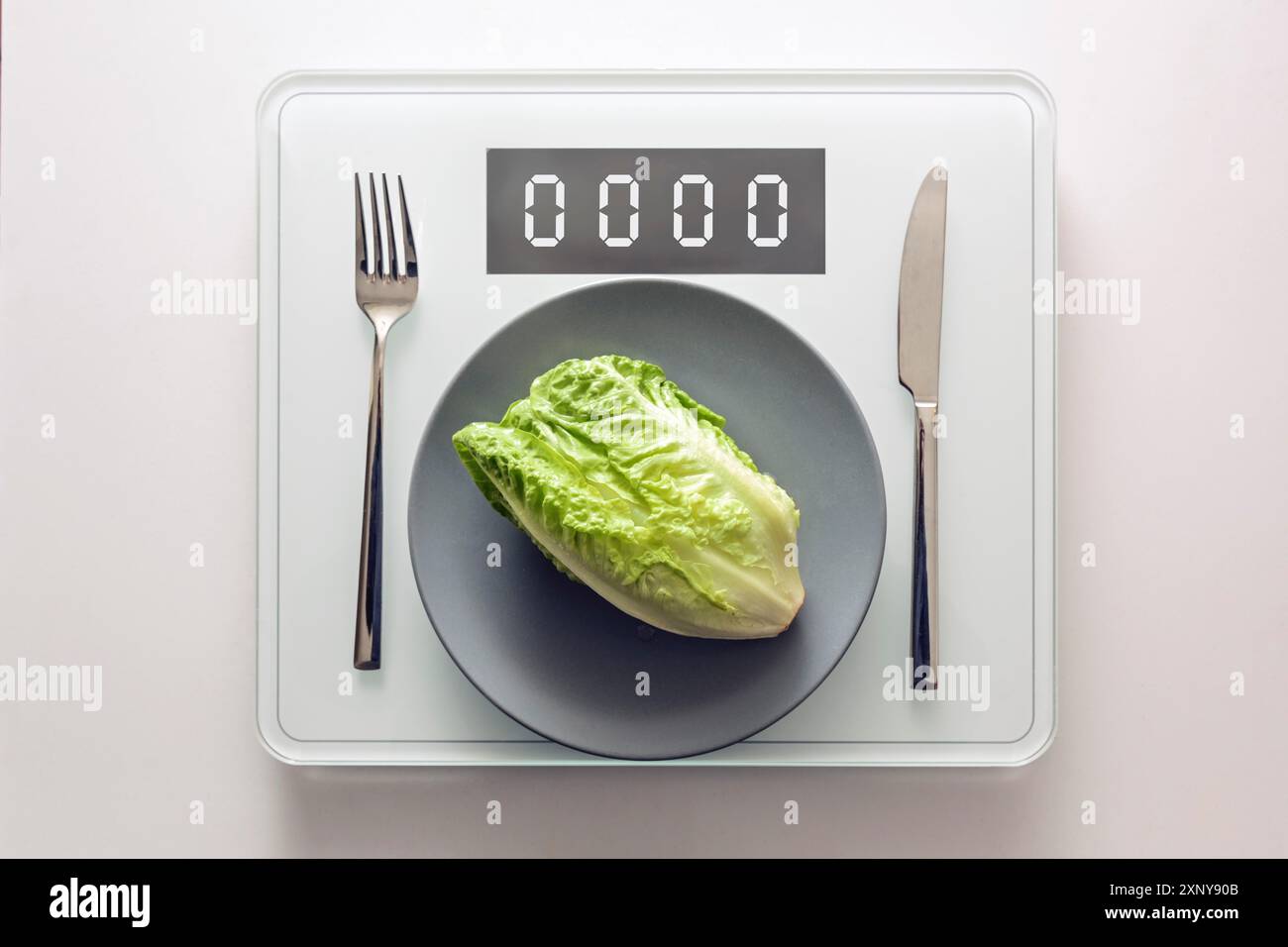 Lattuga verde fresca o baby cos su un piatto grigio e posate su una bilancia digitale che mostra zero, dieta sana e perdere peso concetto, copia spazio Foto Stock