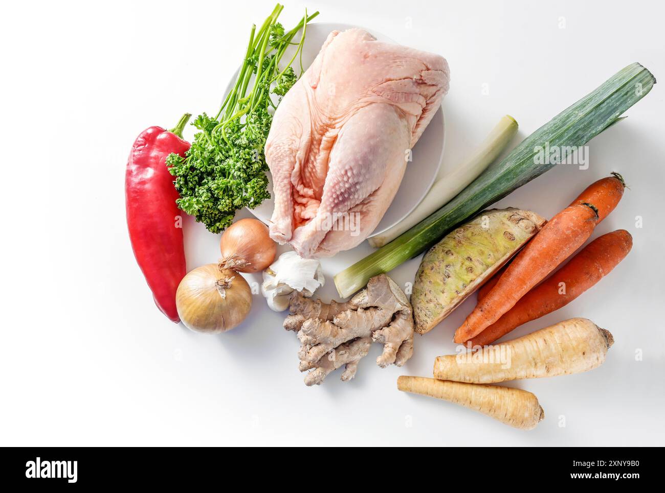 Ingredienti crudi per un sano brodo di pollo contro il raffreddore e l'influenza con verdure a radice, porri, zenzero, cipolla, aglio e peperone rosso su una luce Foto Stock