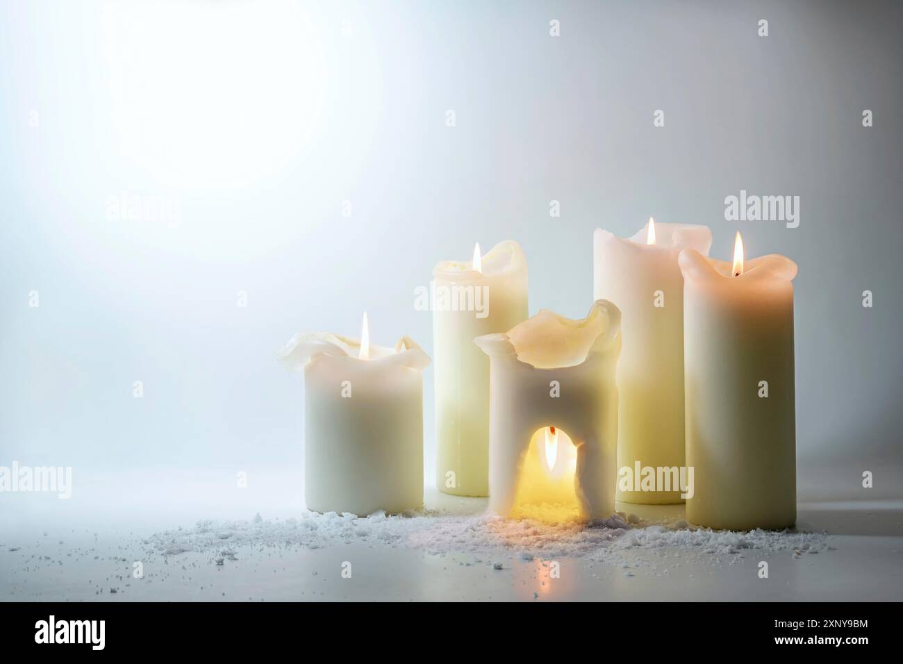 Gruppo di candele bianche, uno sta bruciando sopra la testa in una grotta calda, vita ferma surreale come concetto di risparmio energetico, non sprecare il calore all'esterno, grigio chiaro Foto Stock