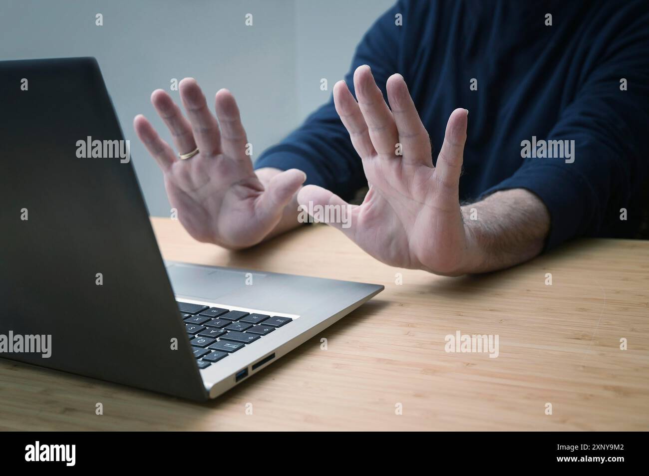 Mani in un gesto difensivo contro un computer portatile, evitando di lavorare ulteriormente su un sistema hackerato o altri pericoli e reati, rischi online per il business Foto Stock