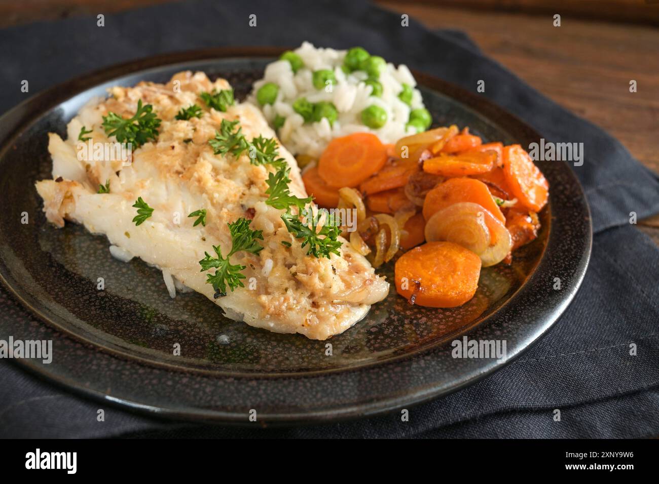 Filetto di merluzzo con contorno di prezzemolo, carote e riso con piselli verdi su un piatto scuro, pasto di pesce sano, focus selezionato, profondità di campo molto ristretta Foto Stock