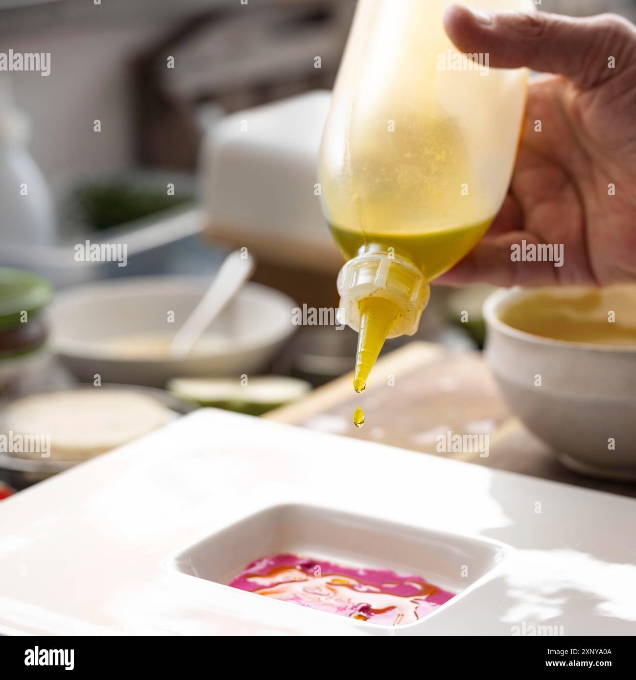 Chef gourmet che versa olio prezioso da una bottiglia in salsa di barbabietole per preparare un menu su un piatto bianco, cucina creativa, selezionata Foto Stock